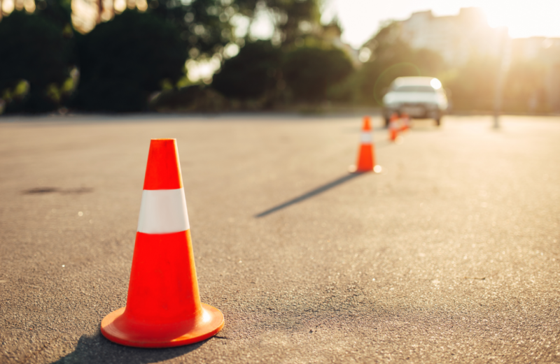 A line of orange traffic cones on an asphalt lot with a blurred car in the background.