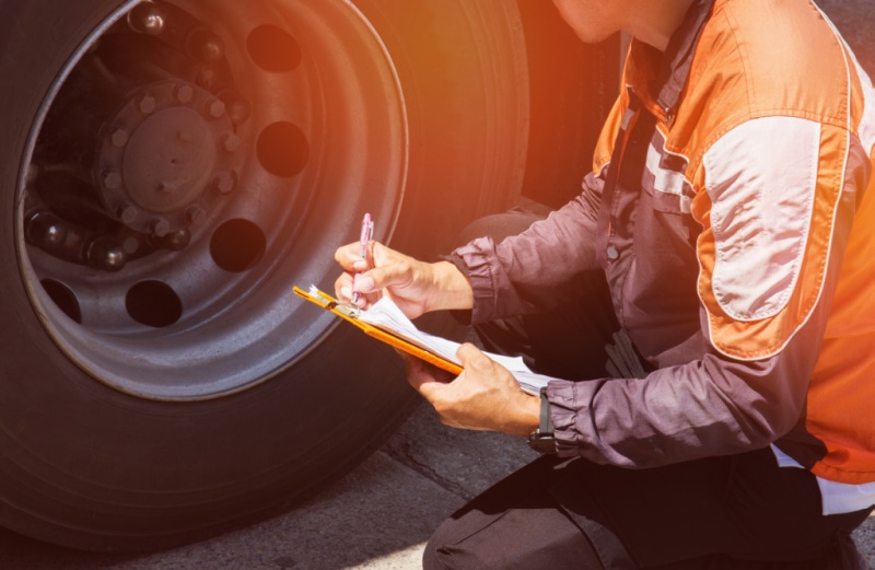 person inspecting a tire on a semi truck while holding a clipboard
