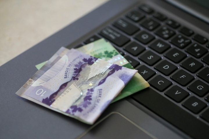 a black laptop with Canadian money sitting on the side of the keyboard.