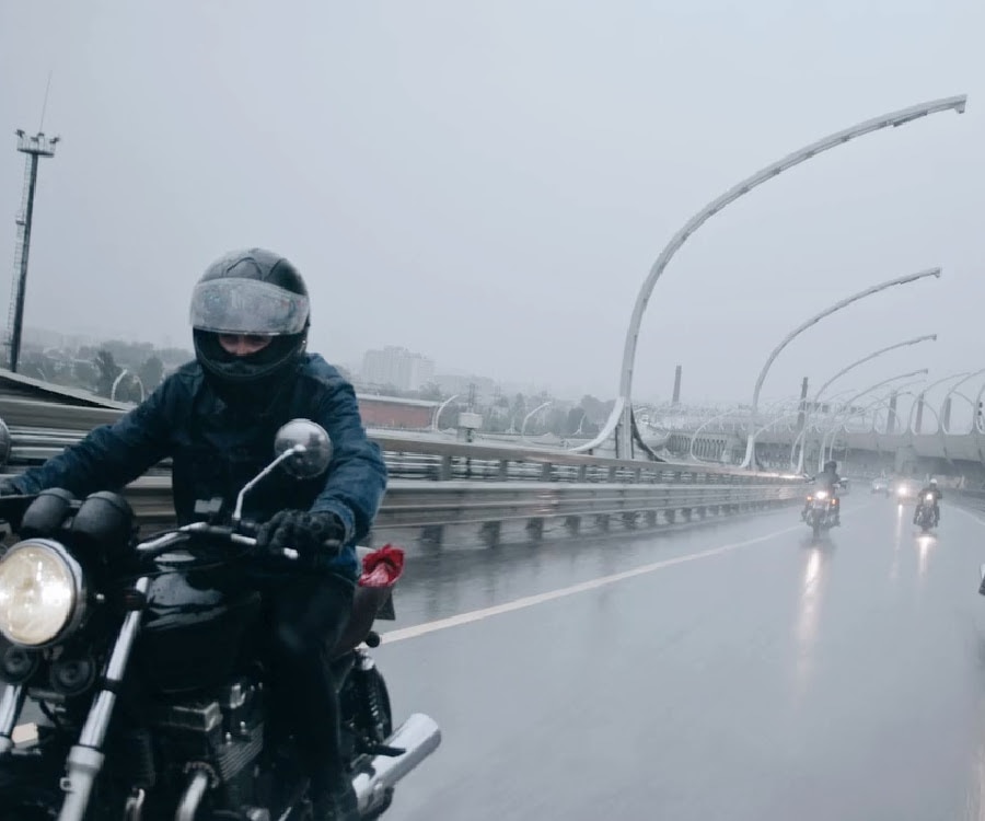 A motorcycle rider on the road with other motorcycle riders following behind.  It is raining.