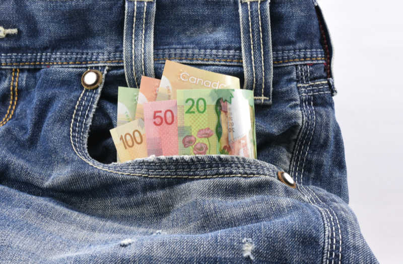 A variety of colorful Canadian bank notes, including 20, 50, and 100 dollar bills, tucked into the front pocket of a pair of blue jeans.
