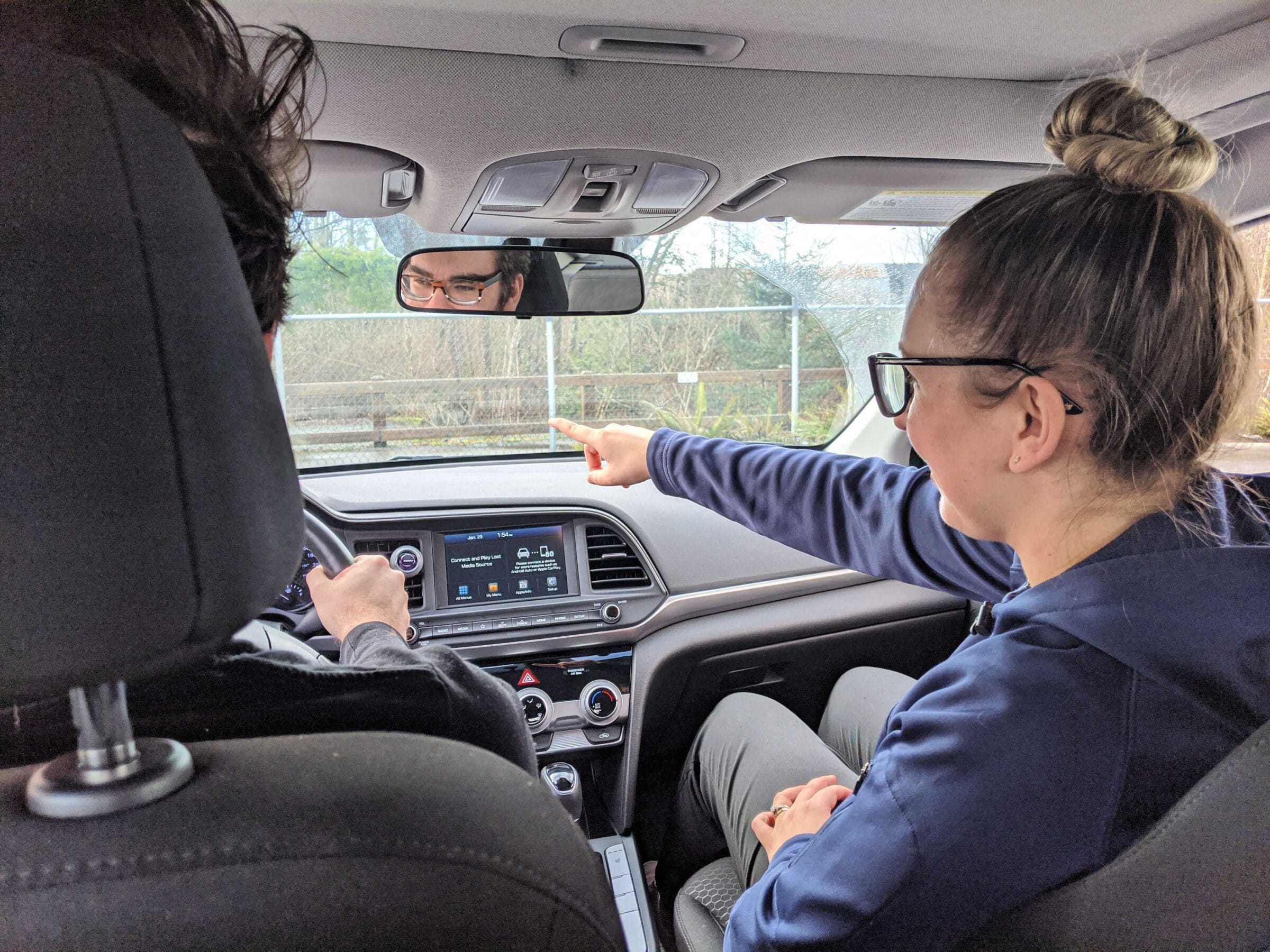 view from the back seat of a car. a woman in the passenger seat is giving directions to the driver.