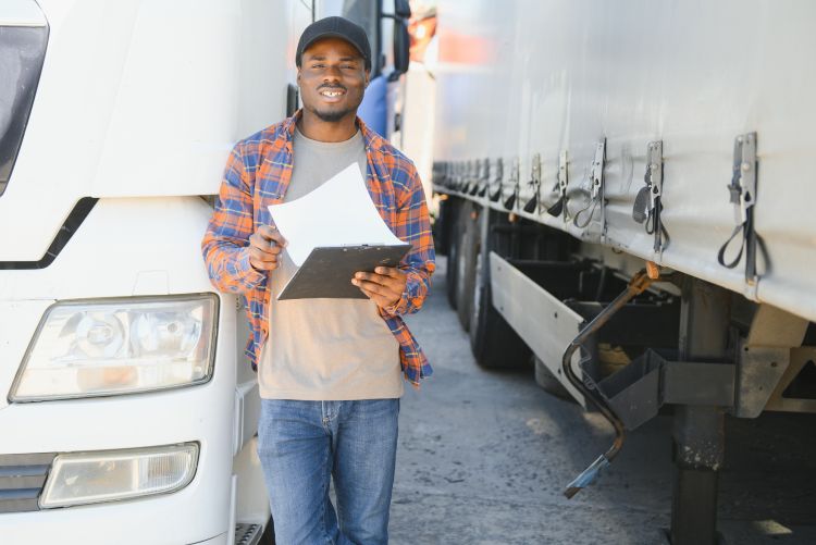 Man standing beside a white semi truck, holding a clipboard and smiling.