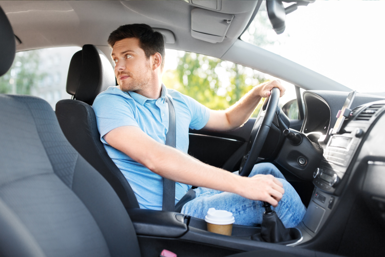 A man in a light blue button-down shirt sitting in the driver's seat of a car, looking over his shoulder while reversing.