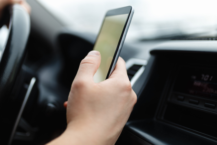 A person holding a smartphone while sitting in the driver's seat of a car.