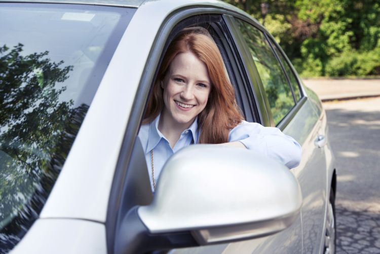 Woman leaning out the driver's side window of a white car, smiling.