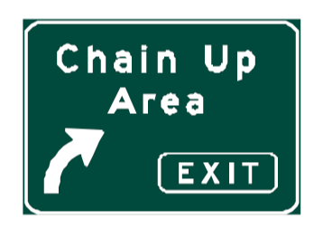 A green rectangular sign with a white border that reads Chain Up Area with a white arrow pointing to the right and a smaller black and white EXIT sign below it.