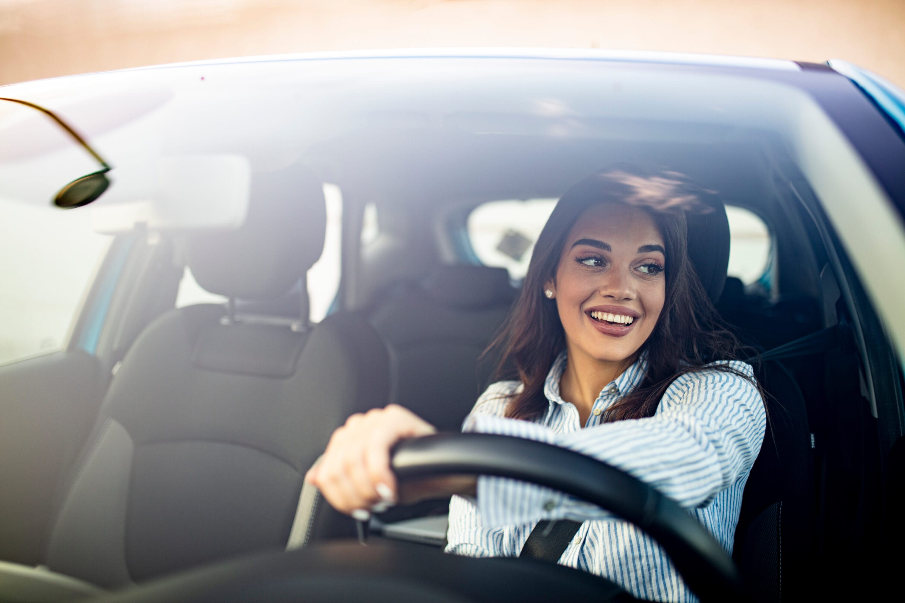 a woman is smiling while driving a car with one hand on the wheel.