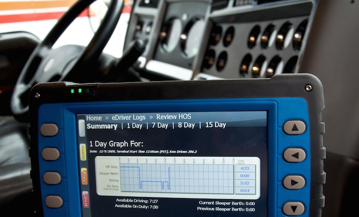 A close-up of a digital electronic logging device (ELD) inside a truck cab displaying a driver's hours-of-service graph.