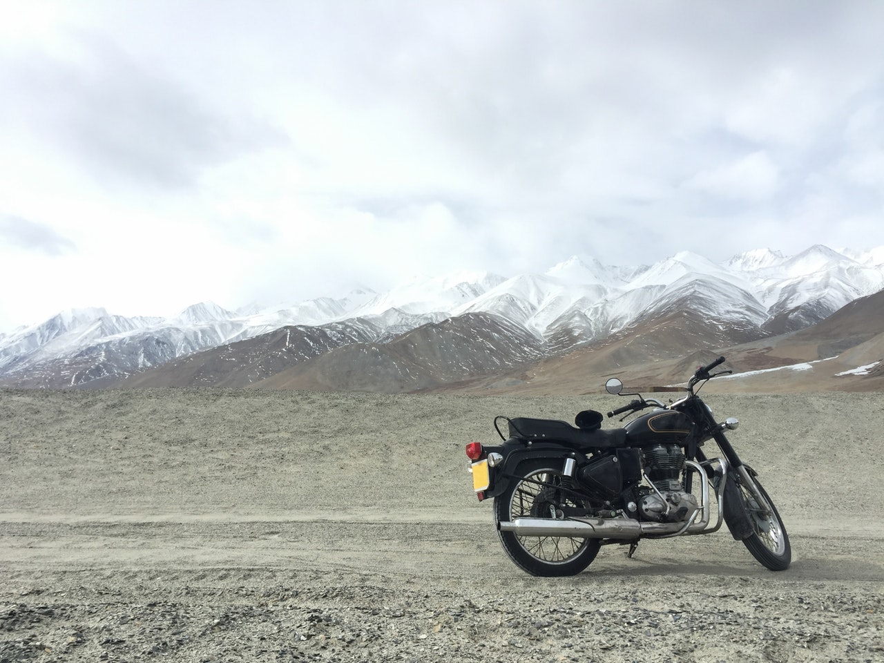 A black motorcycle parked on a gravel surface with a vast landscape of snow-capped mountains in the background.