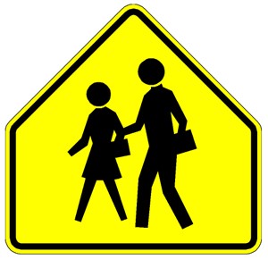 A yellow pentagon-shaped school zone sign featuring silhouettes of two people walking.