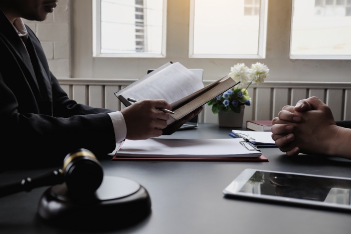 a lawyers office with a man reading from a book with a gavel and iPad sitting on the desk next to him.