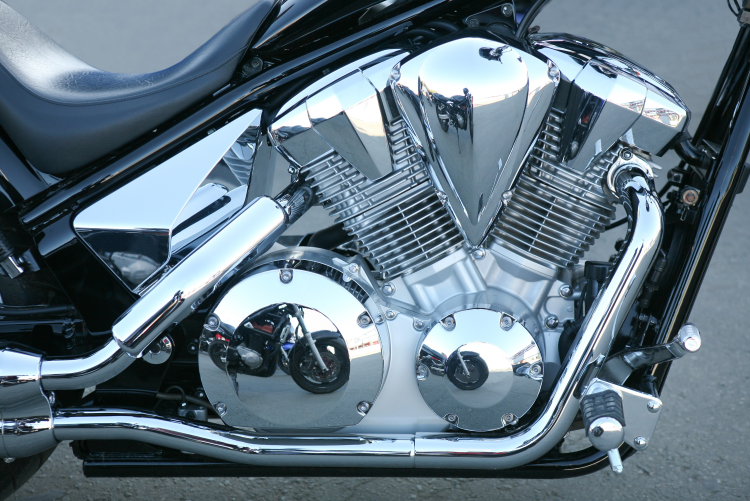 A detailed close-up of a polished chrome V-twin motorcycle engine, showcasing the gleaming reflective surfaces, cooling fins, and exhaust pipes.