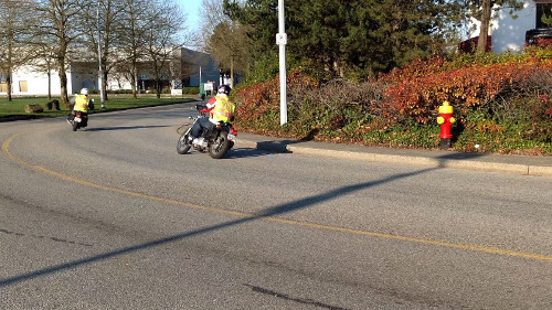 Two motorcyclists in bright yellow safety vests navigate a curve on an asphalt road.