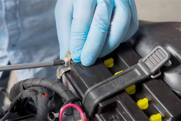 A close-up of a person wearing blue gloves using a screwdriver to adjust a terminal on a battery, which is secured by a black strap.
