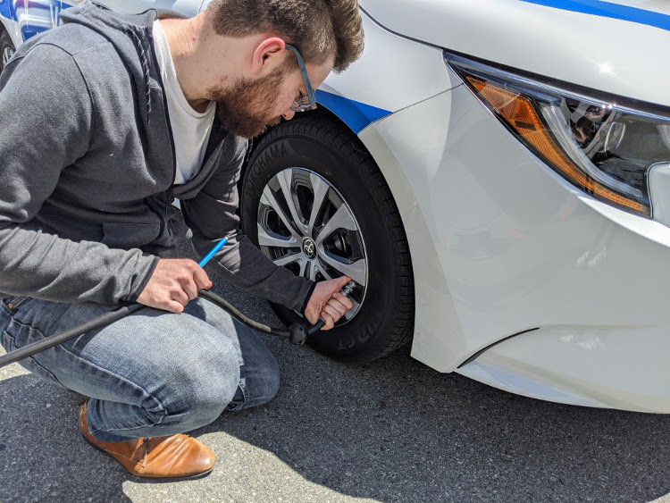 A man using an air hose to inflate a tire on a branded Valley Driving School vehicle.