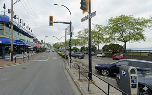 An intersection on Marine Drive in White Rock showing a parking lot to the right on the road and local business on the right side of the road.
