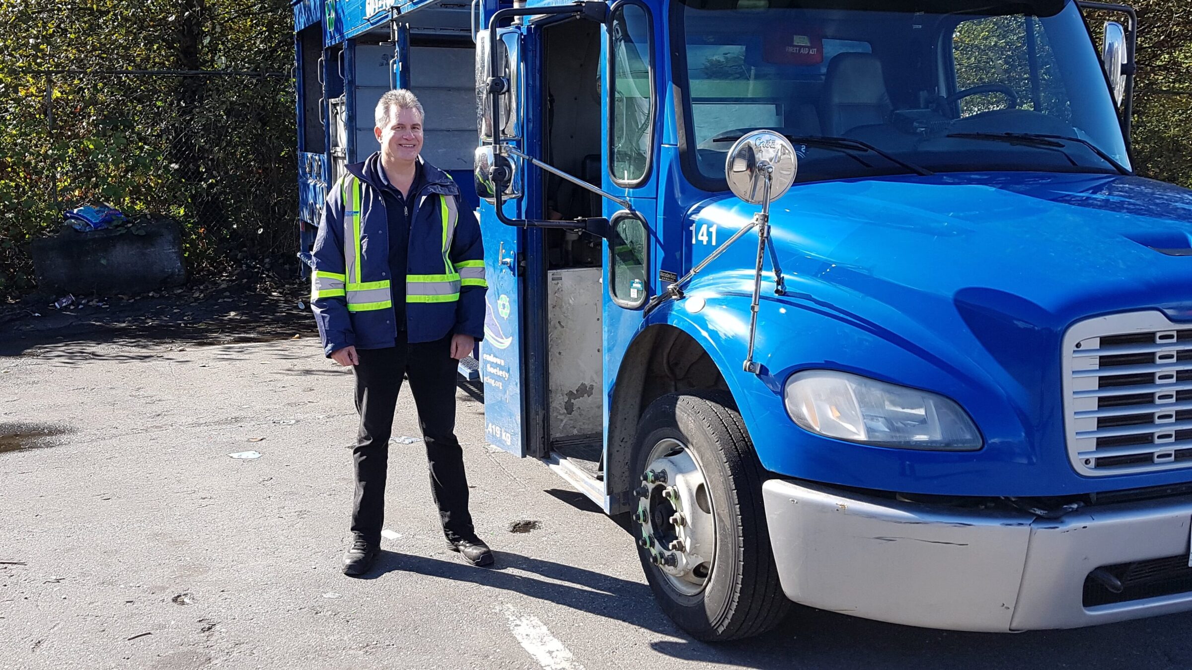 A man standing beside a blue recycling truck.