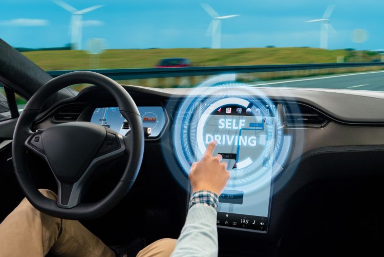 A photo showing the interior of a vehicle from the driver's perspective, focusing on the steering wheel, hands-on control, and the digital dashboard display visualizing the road ahead, illustrating the interface of an assisted or automated driving system.